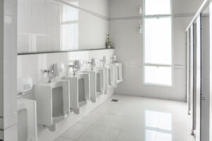 White urinals in clean men public toilet room empty with big window and light from outside, interior.